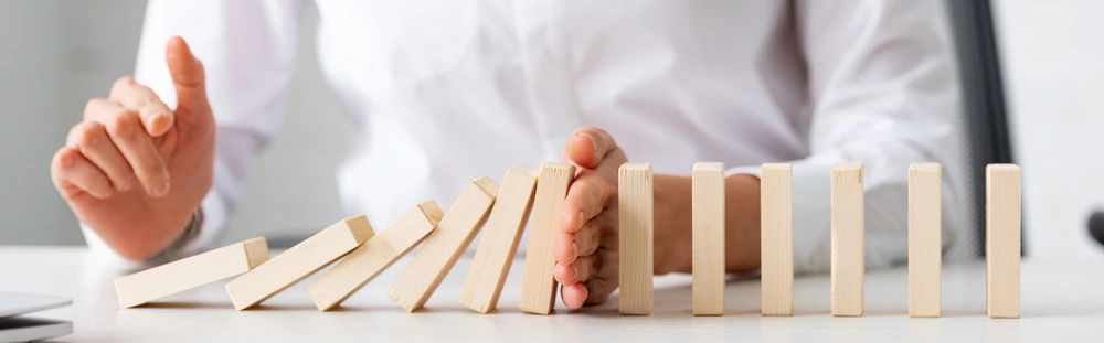 © LIGHTFIELD STUDIOS / Adobe Stock Eine Person stoppt mit der Hand die fallenden hölzernen Dominosteine.